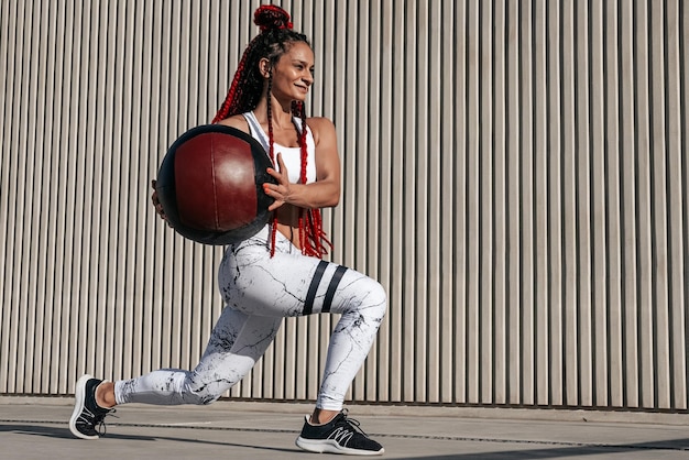 Wysportowana kobieta robi ćwiczenia z wypadu z piłką lekarską Siła i motywacja Zdjęcie wysportowanej kobiety w modnej odzieży sportowej