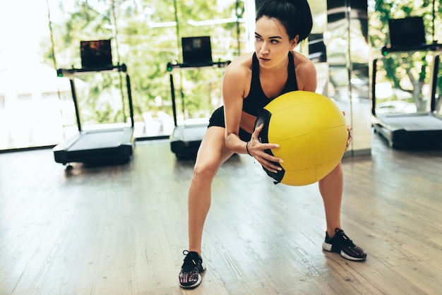 Wysportowana kobieta robi intensywny trening rdzenia w siłowni z piłką lekarską Silna kobieta robi podstawowe ćwiczenia z piłką lekarską w klubie fitness Ludzie sportu i koncepcja stylu życia