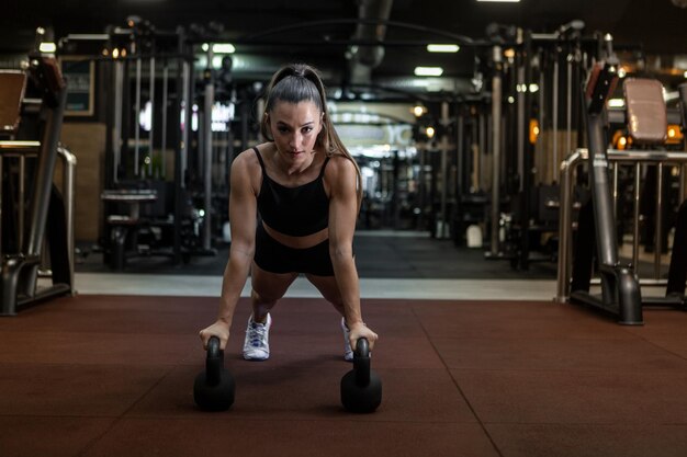 Wysportowana Kobieta Używa Kettlebells Podczas ćwiczeń Deski Na Siłowni