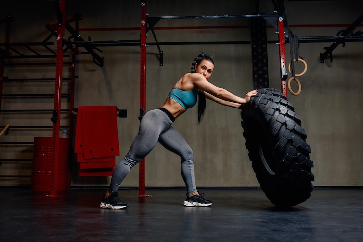 Zdjęcie wysportowana lekkoatletka ćwicząca z ogromną oponą obracającą się i przerzucającą na siłowni kobieta crossfit ćwicząca z dużą oponą