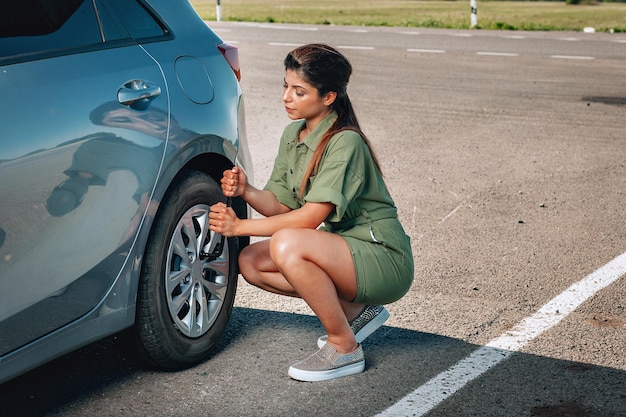 Wysportowana młoda dama naprawia zepsute koło swojego samochodu kluczem nasadowym na parkingu