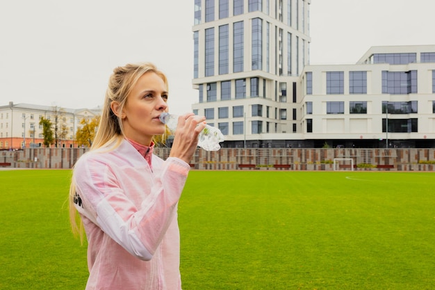 Wysportowana młoda kobieta pije wodę podczas treningu na zewnętrznym stadionie Modelka w dresie