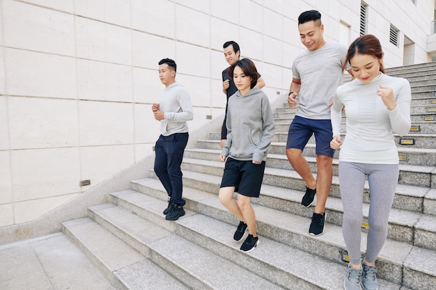 Wysportowani młodzi Azjaci mężczyźni i kobiety zbiegają po schodach w mieście podczas porannego treningu do maratonu