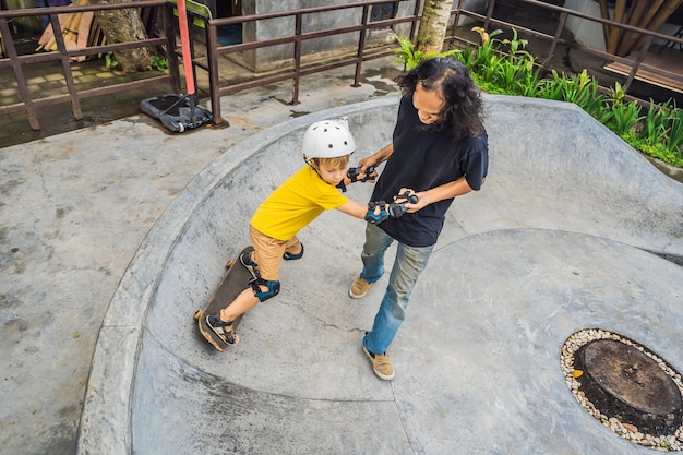 Wysportowany chłopiec uczy się jeździć na deskorolce z azjatyckim trenerem w skateparku Edukacja dzieci Sport Różnorodność ras