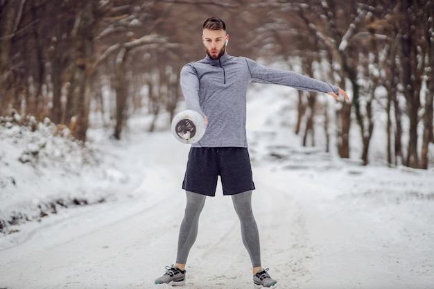 Wysportowany Kulturysta Stojący Na Zaśnieżonej ścieżce W Lesie I Kołyszący Się Kettlebell W Zimie. ćwiczenia Kulturystyczne, Fitness Zimowy, Fitness Na świeżym Powietrzu