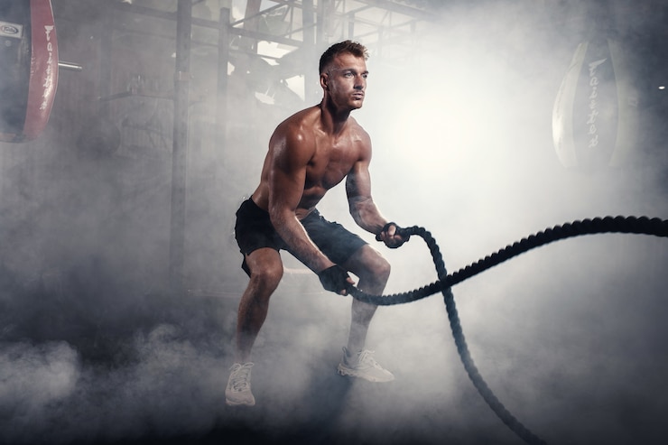 Zdjęcie wysportowany mężczyzna robi ćwiczenia crossfit z liną w zadymionej siłowni