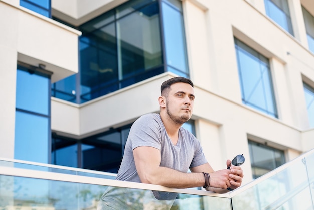 wysportowany mężczyzna w szarej koszulce opiera się o szklaną balustradę na tle budynku