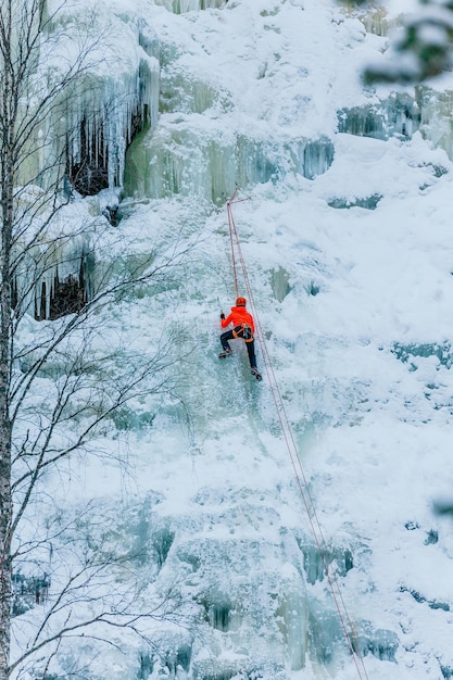 Wysportowany mężczyzna wspinający się po dużej niebieskiej ścianie lodu w Finlandii w Laponii