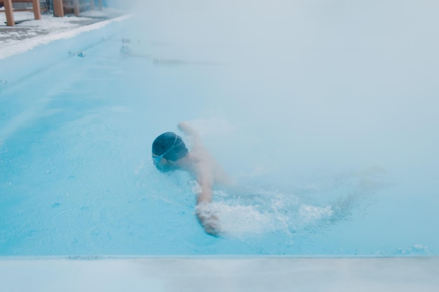 Wysportowany pływak trenujący pływanie w otwartym zimowym basenie z mgłą Koncepcja geotermalnego spa na świeżym powietrzu