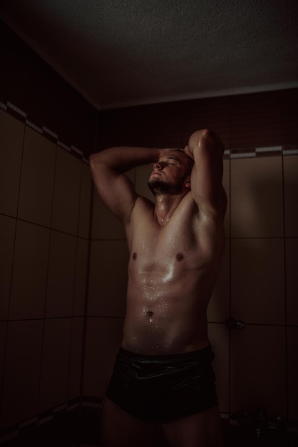 Wysportowany, przystojny i atrakcyjny mężczyzna z umięśnionym ciałem, stojący pod bieżącą wodą w łazience?