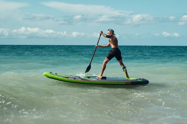 Zdjęcie wysportowany, żylasty surfer pływa z wiosłem na desce w morzu