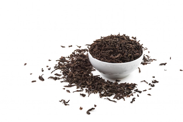 Wysuszeni herbaciani liście w ceramicznej filiżance nad białym tłem.