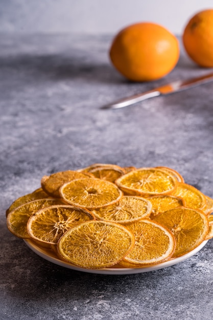 Zdjęcie wysuszeni pomarańczowi owocowi układy scaleni w talerzu na przedpolu i świeżej pomarańczowej owoc na tle