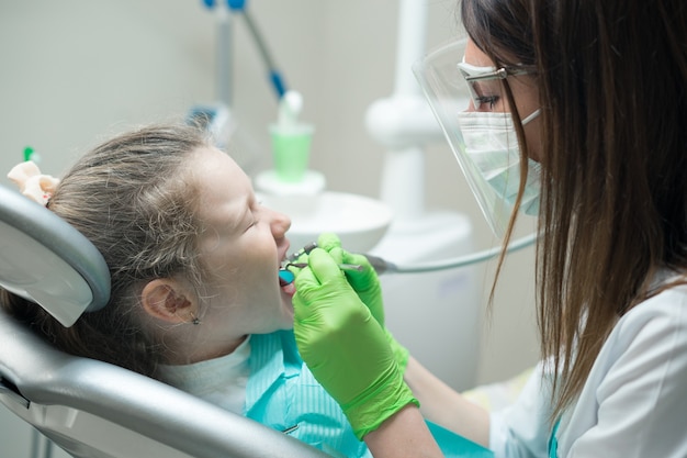 Wyświetlić zbliżenie małe słodkie dziewczyny na fotelu dentystycznym. stomatolog leczący zęby dziecka