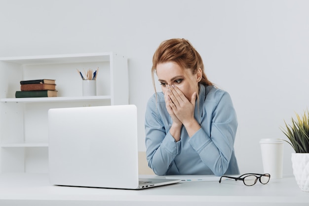 Wyszła kobieta zaskoczona czymś, co ogląda jej laptop w biurze.