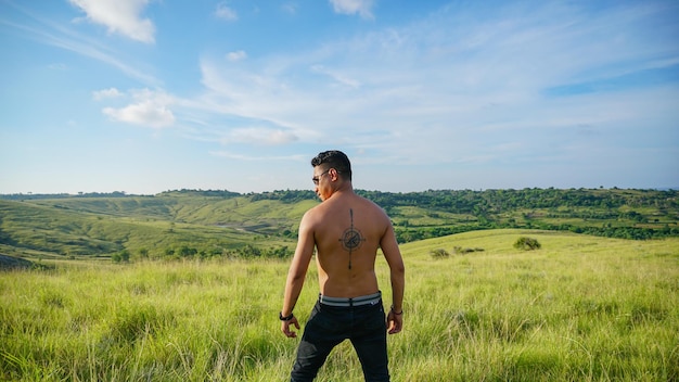 wytatuowany mężczyzna bez ubrania, stojący na zielonej łące