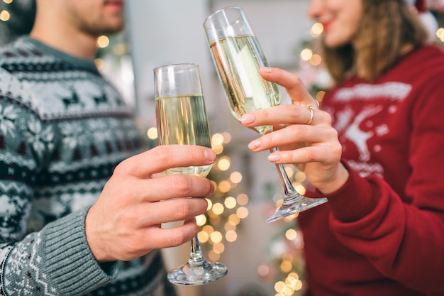 Wytnij widok młodego mężczyzny i kobiety stojących przed sobą. Noszą swetry świąteczne. Para trzyma okulary champaigne. Ona się uśmiecha.
