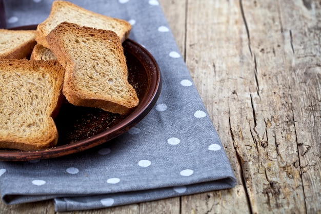 Wznoszący toast zboża chleba plasterki na brown ceramicznym półkowym zbliżeniu na bieliźnianej pielusze na nieociosanym drewnianym stołowym tle.