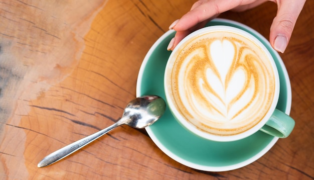 Wzór na powierzchni latte. Wyzwanie dla artysty latte. Widok z góry filiżanka kawy na drewnianym stole. Piękny wzór serca stworzony z mikropianki. Koncepcja kawiarni i kawiarni. Cappuccino kobiece ręce.