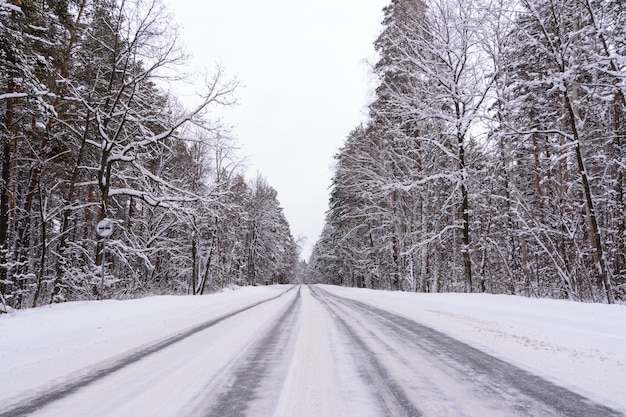 Wzory na zimowej autostradzie w postaci czterech prostych linii. Śnieżna droga na tle ośnieżonego lasu. Zimowy krajobraz.