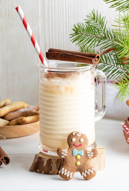 Xmas Eggnog - gorący tradycyjny zimowy napój w szklanym kubku z imbirowym człowiekiem na drewnianym tle.