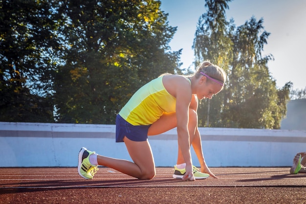 Yong żeński sprinter lekkoatletka przygotowuje się do rozpoczęcia wyścigu na czerwonej bieżni na stadionie lekkoatletycznym.