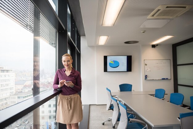 yonug businesswoman w casualowych hipsterskich ubraniach za pomocą smartfona w nowoczesnym wnętrzu sali konferencyjnej w nowoczesnym biurze biznesowym