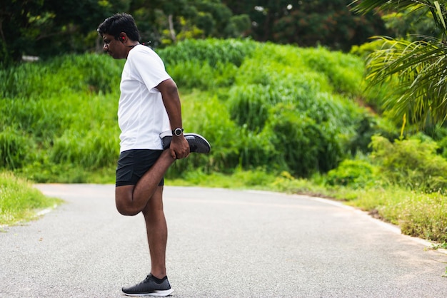 Z bliska azjatycki młody sportowiec biegacz sportowy czarny mężczyzna nosi zegarek podnosząc stopy, rozciągając nogi i kolana przed bieganiem w parku zdrowia na świeżym powietrzu, zdrowe ćwiczenia przed koncepcją treningu
