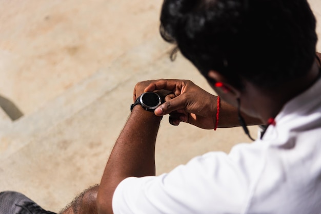 Z bliska azjatycki młody sportowiec sportowiec biegacz czarny mężczyzna nosi nowoczesny inteligentny zegarek siedzi odpoczywa przed treningiem biegając w parku zdrowia na świeżym powietrzu, zdrowe ćwiczenia przed koncepcją treningu