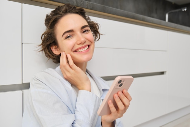 Zdjęcie z bliska portret szczęśliwej kobiety z telefonem w domu, dotyka twarzy i lekko się uśmiecha