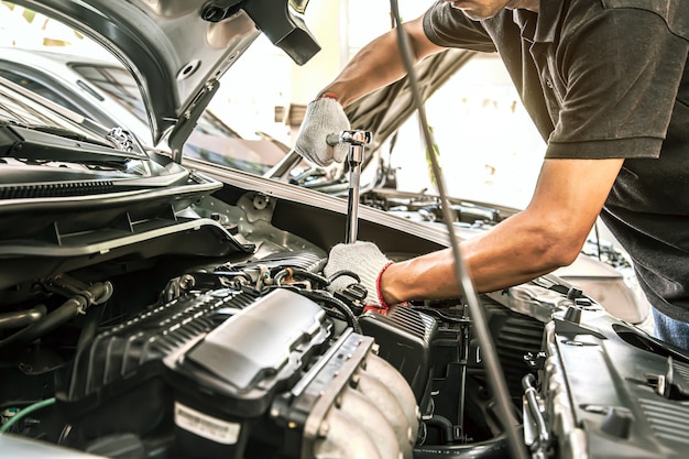 Z bliska ręce mechanika samochodowego używają klucza do naprawy silnika samochodu.