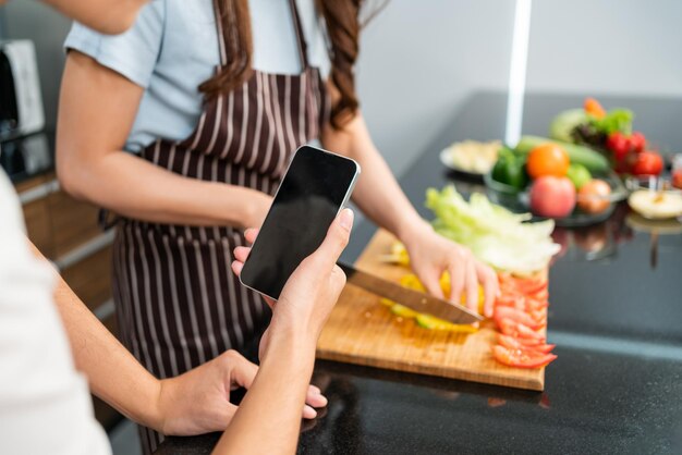 Zdjęcie z bliska ręce mężczyzny na żywo przez telefon komórkowy podczas gdy kobieta przygotowuje wegetariańską zdrową sałatkę