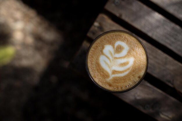 Z bliska strzał czarnej kawy gorące cappuccino z kwiecistą latte art na drewnianym stole pod