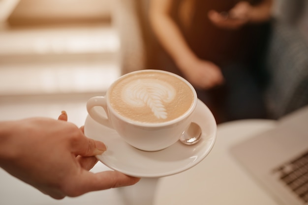 Z bliska zdjęcie latte, które kobieta-barista podaje dziewczynie w kawiarni.