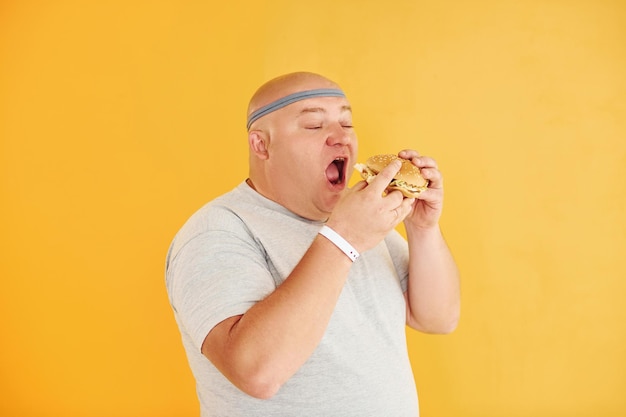 Z fast foodem Zabawny mężczyzna z nadwagą w sportowym krawacie jest na żółtym tle