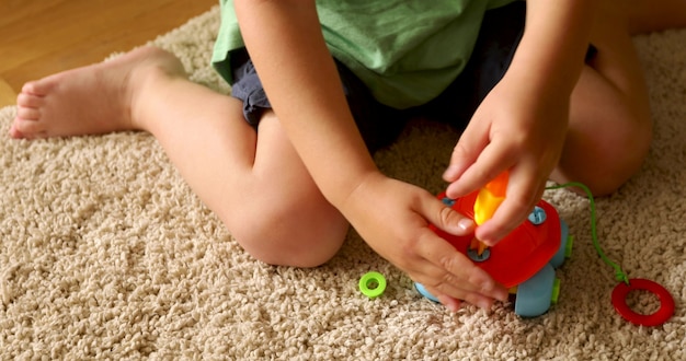 Z góry nie do poznania dziecko bawiące się zabawką siedzącą na dywanie na podłodze w domu