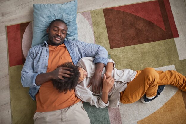 Z góry ujęcie kochającego Afroamerykańskiego ojca, który relaksuje się na podłodze w domu ze swoim młodym synem