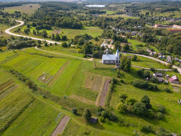 Z góry widok małej wioski pośrodku zielonego pola i lasu Stary kościół na wzgórzu w centrum miasta Widok lotniczy pola rolniczego i krajobrazu naturalnego