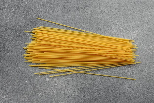 Z góry widok surowej surowej makaronu spaghetti ułożonego w porządny wiązek na szarym kamiennym tle z teksturą Prosta kompozycja podkreślająca teksturę i kolor suchego makaronu