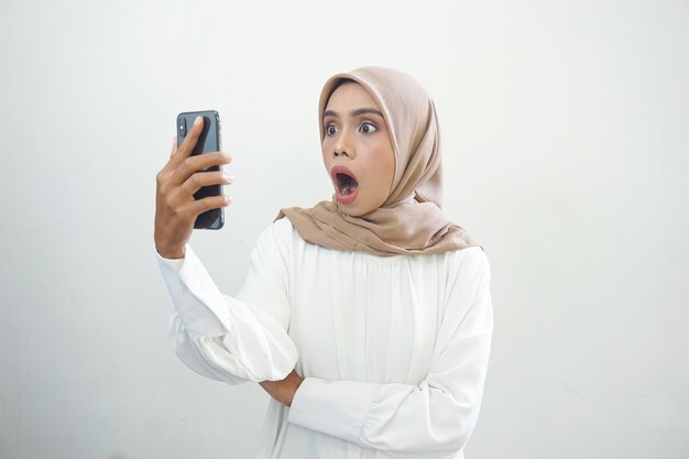 Z podnieceniem piękna azjatycka muzułmańska kobieta pokazuje telefon komórkowego odizolowywającego nad białym tłem