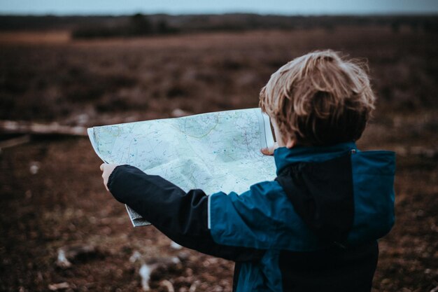 Zdjęcie z tyłu chłopiec trzymający mapę, stojący na polu