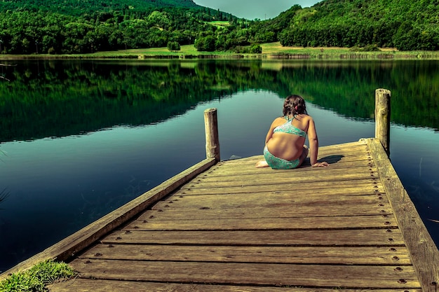 Zdjęcie z tyłu dziewczyna siedząca na molo nad jeziorem