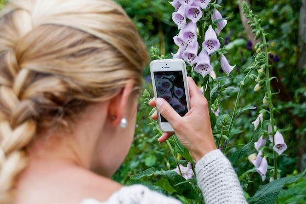 Zdjęcie z tyłu młoda kobieta fotografuje kwiaty za pomocą telefonu komórkowego