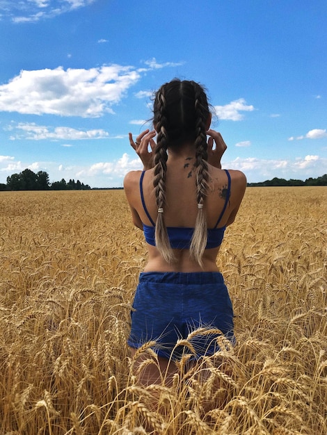 Z tyłu młoda kobieta z warkoczami na polu pszenicy