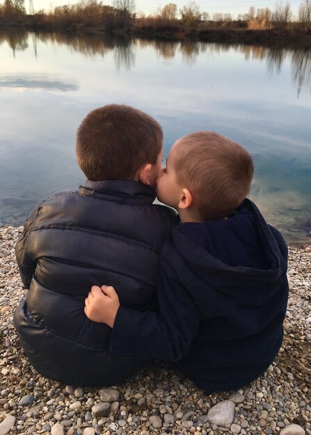Zdjęcie z tyłu widok chłopca całującego brata, siedzącego nad jeziorem