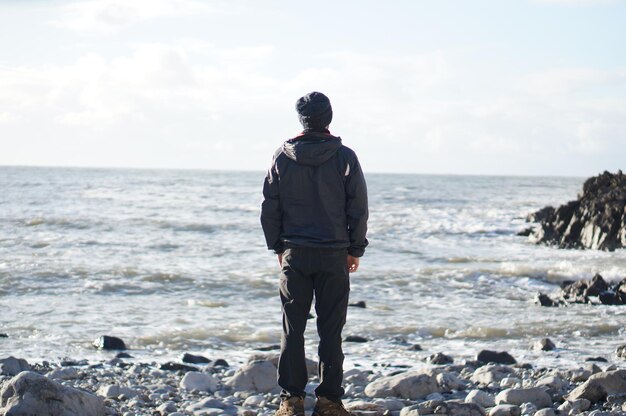 Z tyłu widok człowieka patrzącego na morze, stojącego na skale na plaży