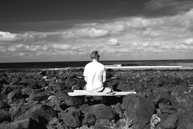 Zdjęcie z tyłu widok człowieka siedzącego na skałach na plaży