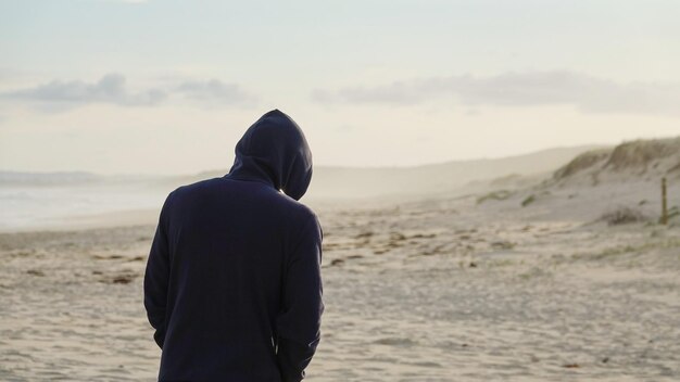 Z tyłu widok człowieka stojącego na plaży na tle nieba