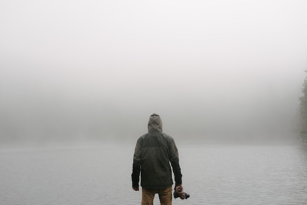 Zdjęcie z tyłu widok człowieka stojącego przed jeziorem w mglistą pogodę