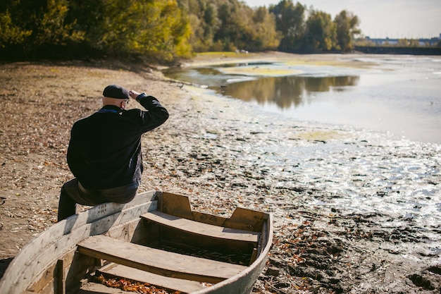 Zdjęcie z tyłu widok dojrzałego mężczyzny siedzącego na łodzi na brzegu jeziora w lesie
